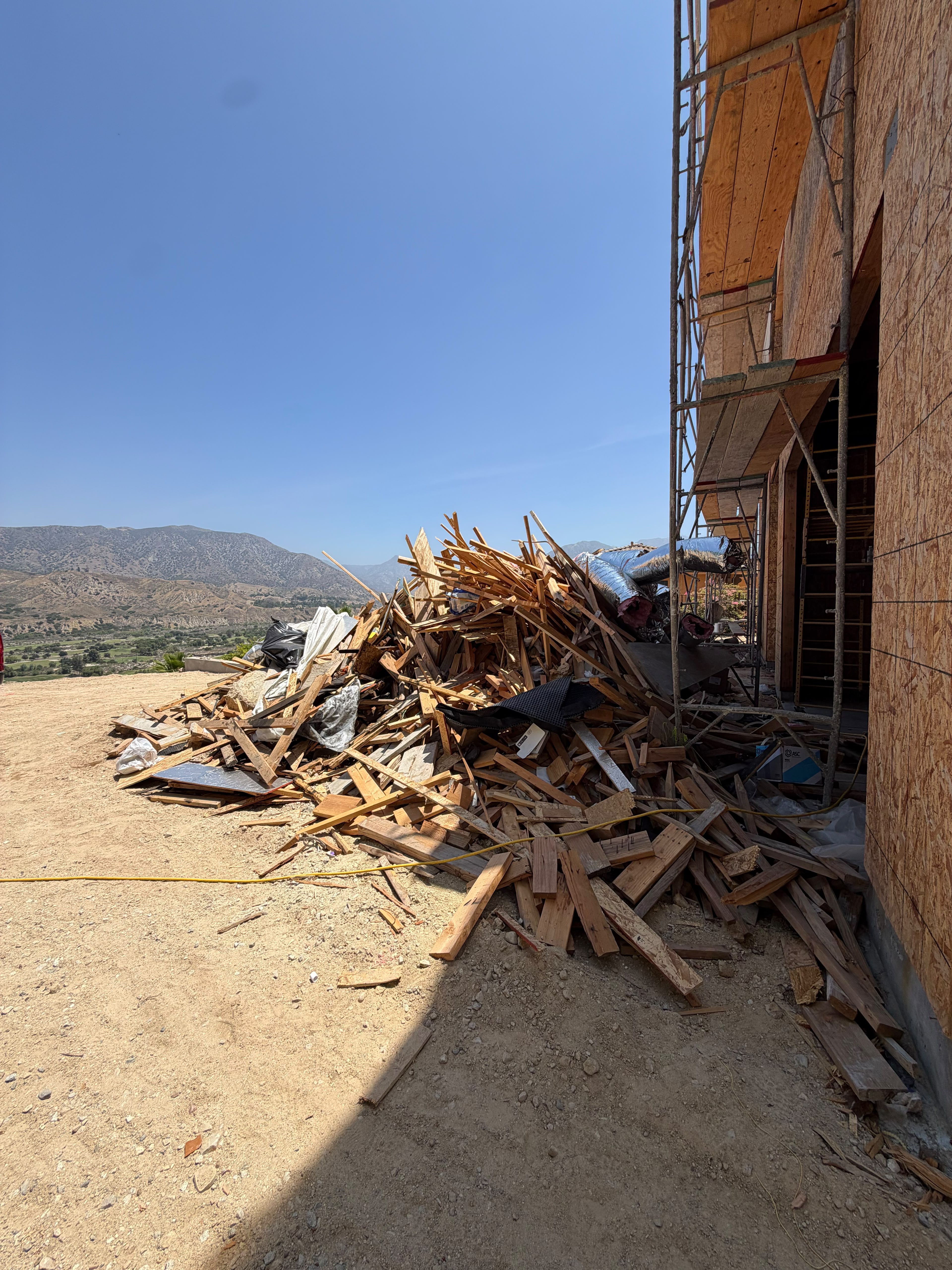 Pile of wood construction debris beside unfinished building and scaffolding