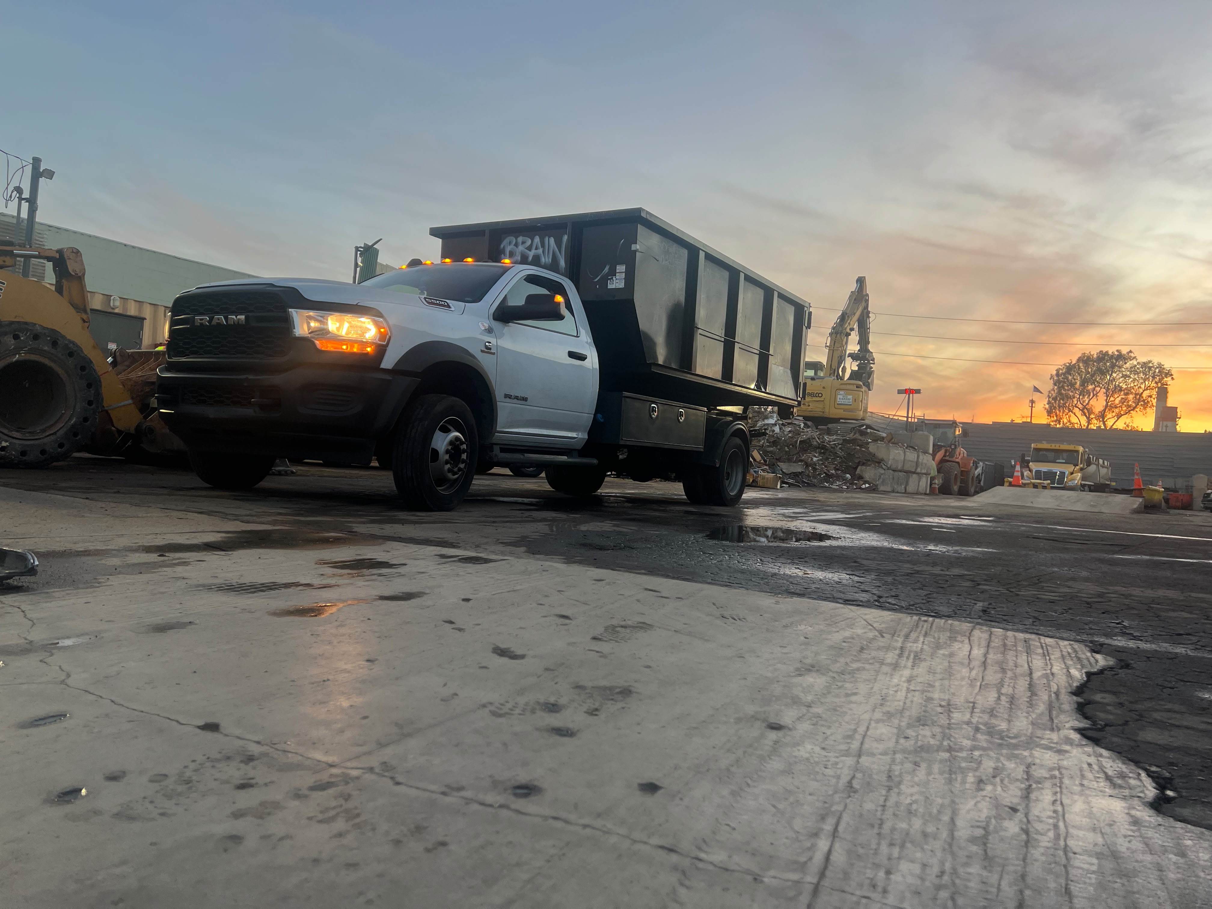 White roll-off dumpster truck at a scrapyard during sunset