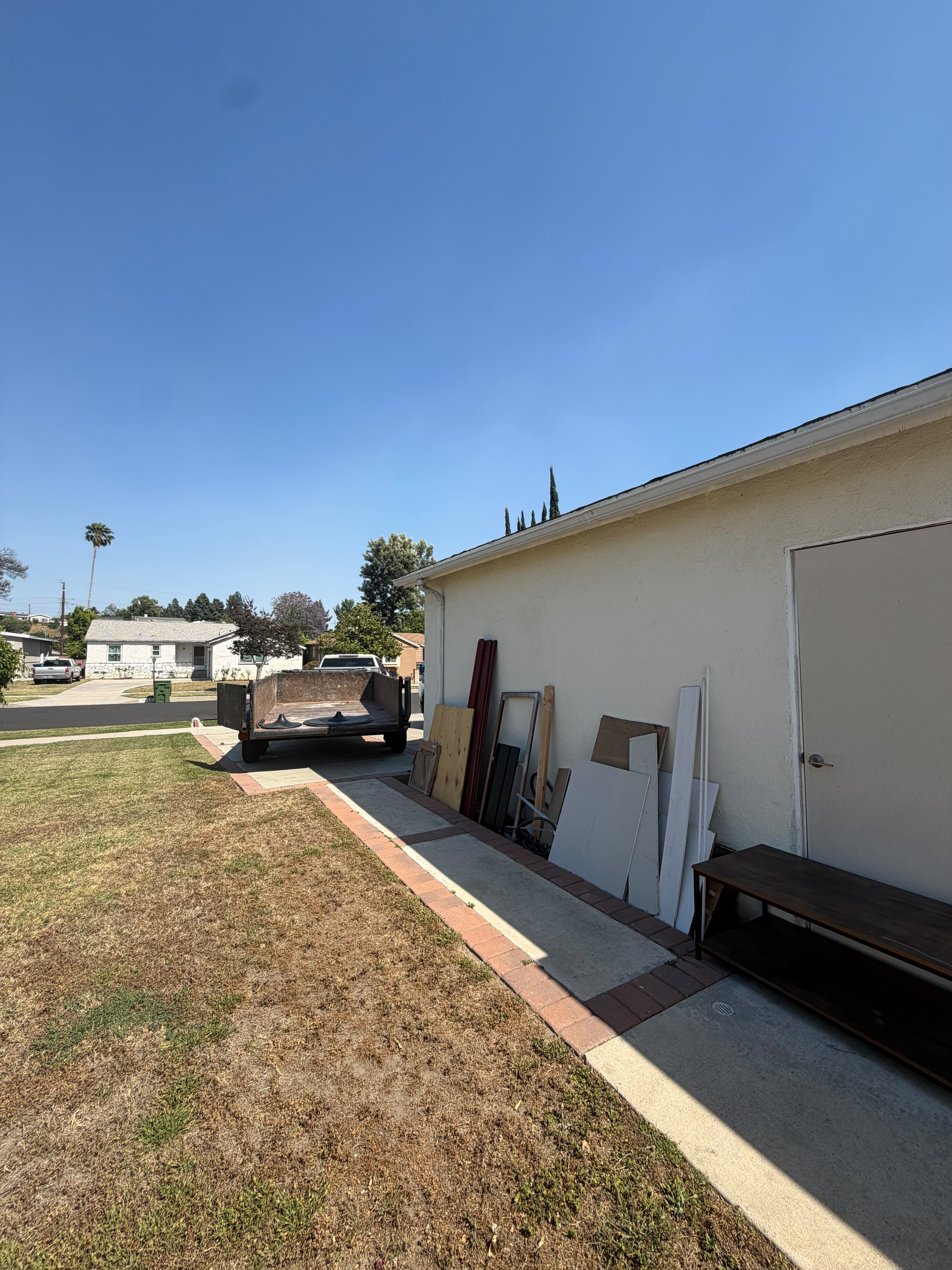 Trailer beside house with wood panels, shelving unit, and debris for removal