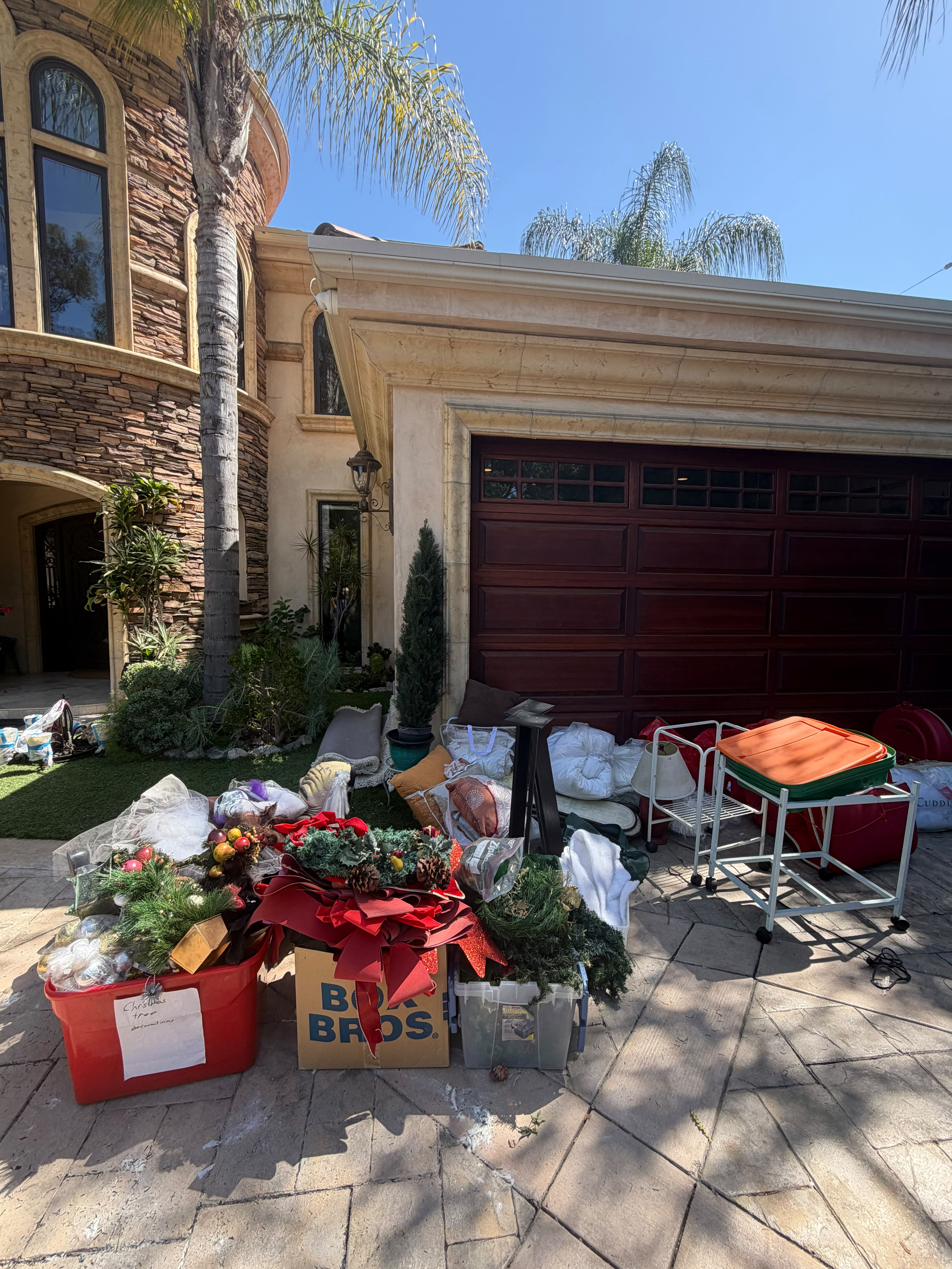 Holiday decorations, storage bins, and assorted clutter piled in driveway by garage